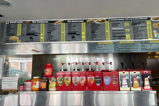 Photo de l'intérieur de la friterie. On voit notamment le menu avec en dessous le présentoir des sauces