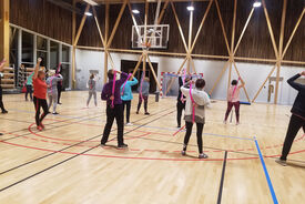 Photo d'un groupe de personnes dans la salle de sport, debout en train de faire des exercices d'étirement des épaules avec des élastiques